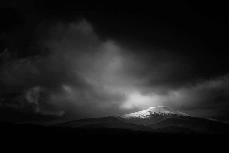 Runner up - Landscape category - Scottish Landscape Photographer of the Year. I shot this image during a pit-stop at the Commando Memorial at Spean Bridge. I was admiring the bronzed soldiers view of the mighty Nevis range to the south, the hills encased in a thick layer of snow. As my eye turned west I was stuck by the lovely profile of Stob a Ghrianain rising above a thick strip of pines. The soft and thick cloud formations moving over the scene made for a perfect backdrop to the crisp lines and contrasts created by the strong sunlight and I accentuated the mood in post processing by taking the exposure down to draw you in to the spill of light on the peak.